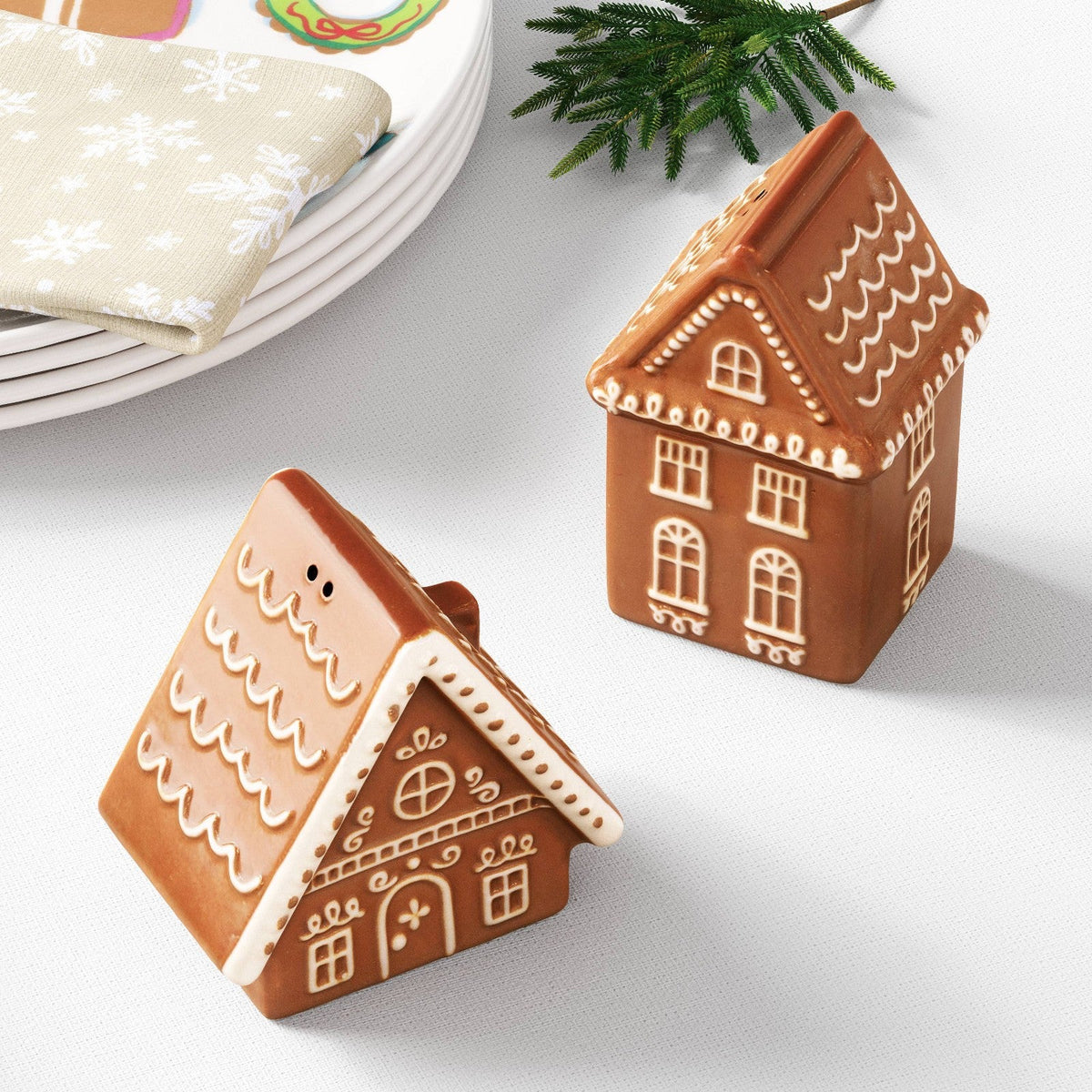 Salero y pimentero Wondershop de casas de jengibre sobre mesa junto a platos y una ramita navideña