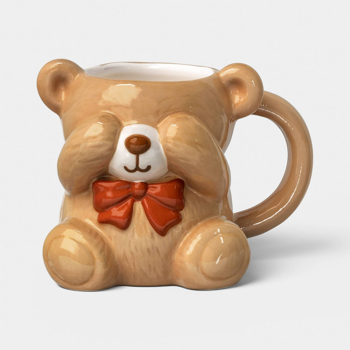 Mini taza de cerámica Wondershop en forma de oso cubriéndose los ojos y moño rojo, vista frontal #tamaño_222 ml / 7.5 fl oz